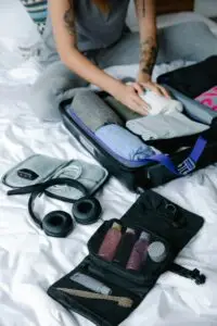 Person organizing suitcase with clothes and toiletries on bed, preparing for travel.